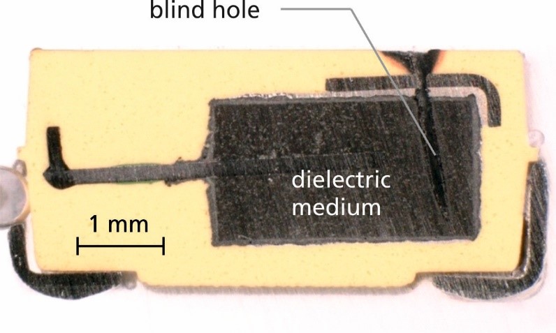 Cross section of a tantalum capacitor. The arrow indicates the blind hole generated by laser ablation to access the dielectric medium.